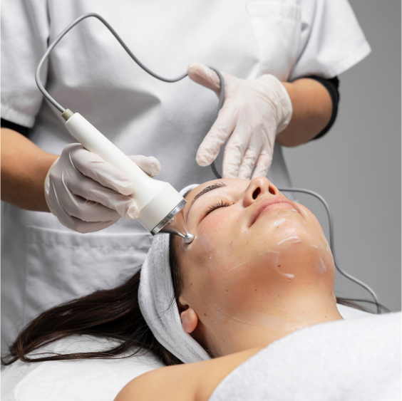 A dermatologist performing a Bela MD facial treatment on a patient lying on a medical bed. The dermatologist is wearing scrubs and white surgical gloves while applying the procedure to the patient’s face.