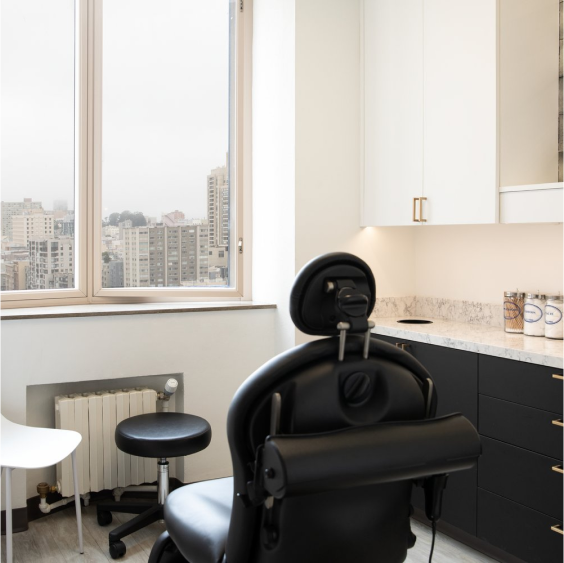 Consultation room of Dr. Caren Cambell featuring the examination chair and a large window in front, creating a bright and welcoming space for dermatological evaluations.