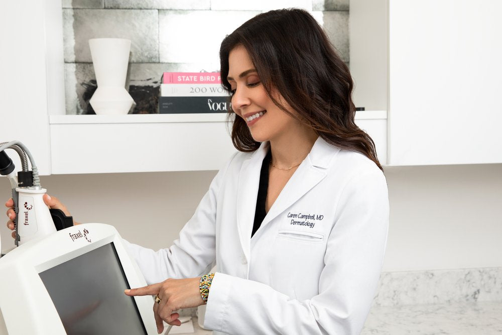 Dr. Caren Campbell in her dermatology office, wearing a white coat and demonstrating the Fraxel machine, a state-of-the-art device used for skin resurfacing and rejuvenation treatments