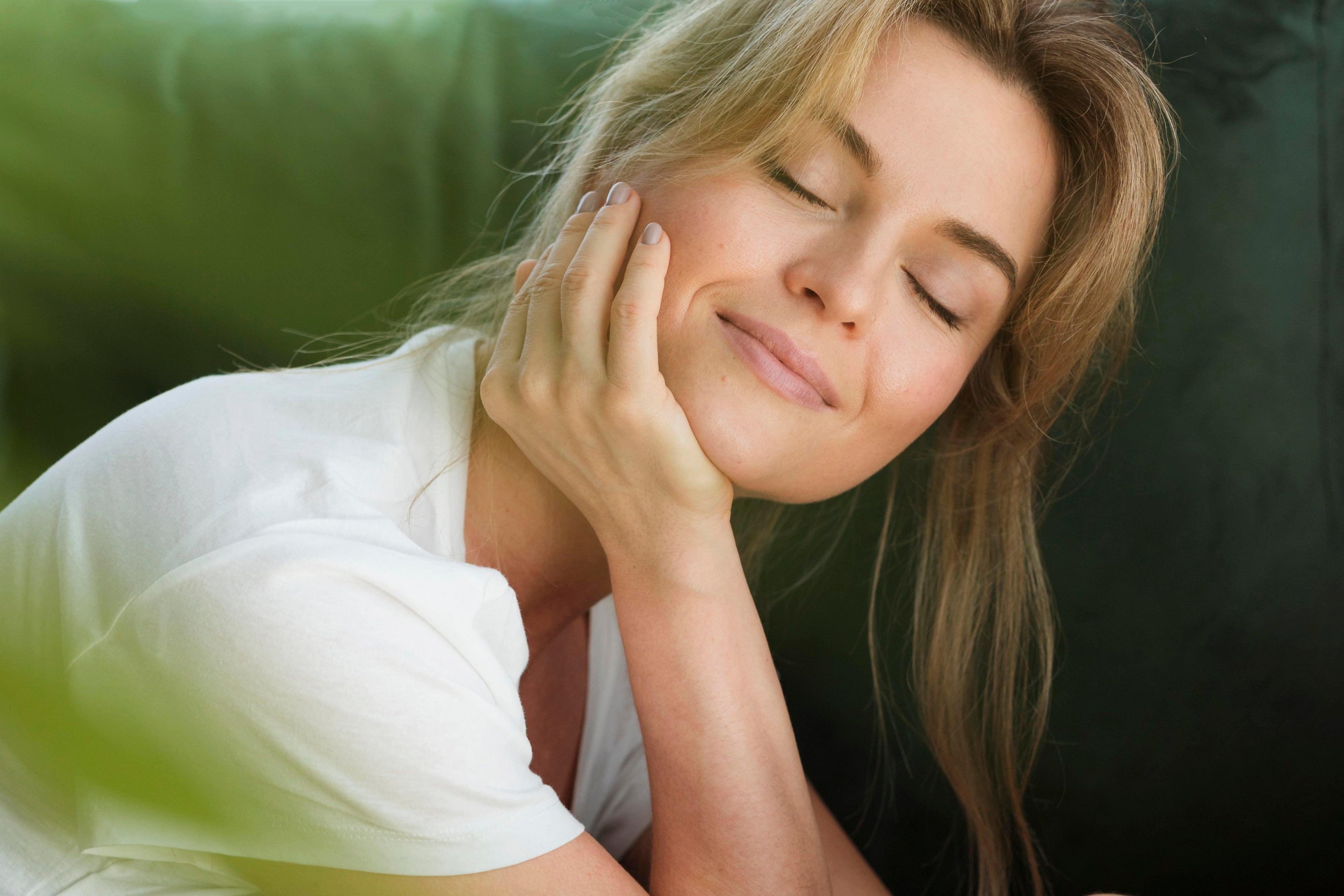 A young blonde woman with fair skin smiling and resting her hand on her chin. The image features the phrase 