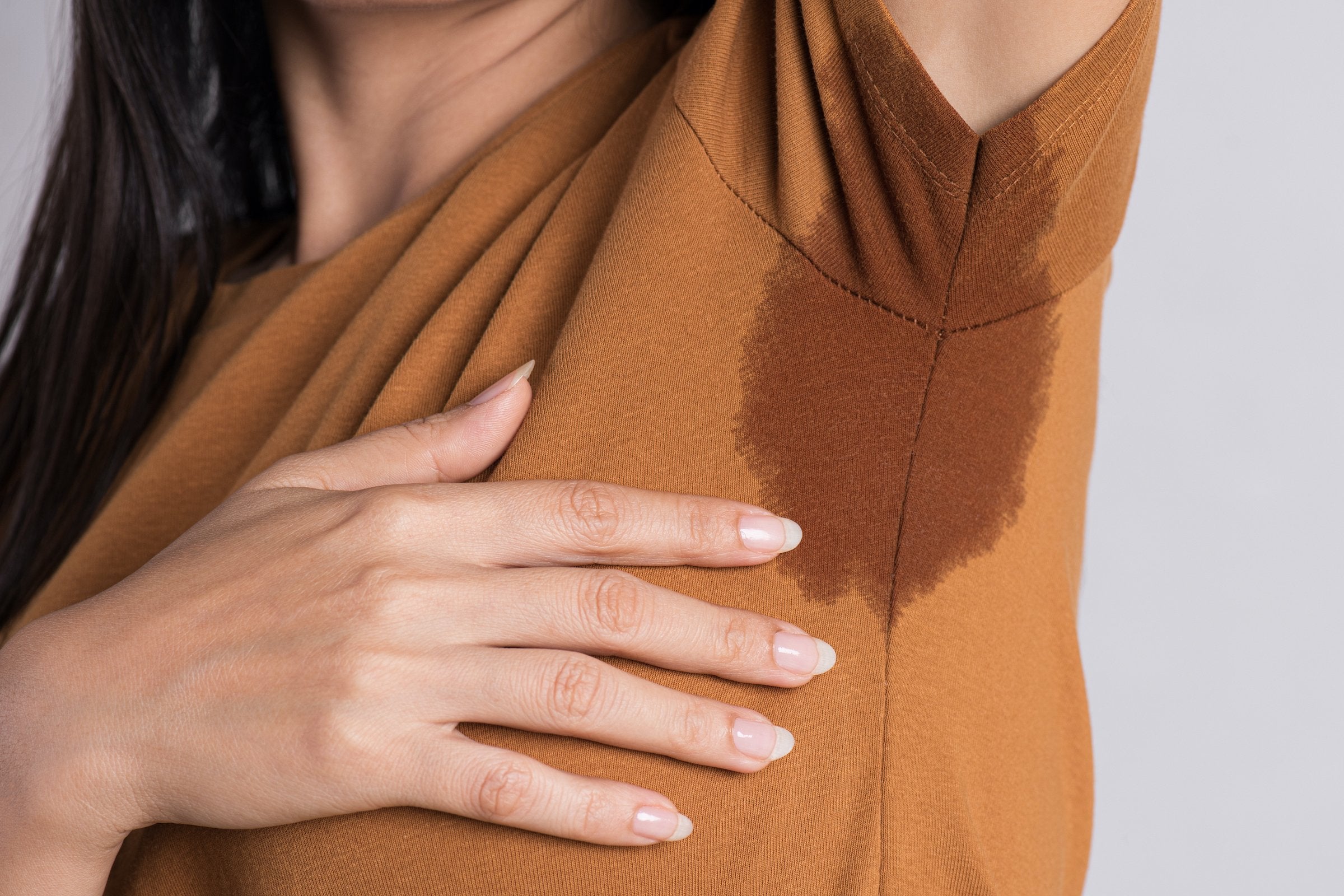  A woman wearing a mustard yellow shirt with visible armpit sweat stains, highlighting the signs of excessive sweating (hyperhidrosis). This image emphasizes the importance of dermatological treatments for managing excessive perspiration.